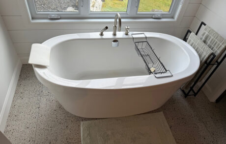 Photo d’une salle de bain neuve avec baignoire autoportante blanche sous la fenêtre, robinetterie chromée, tablette de bain et porte-serviettes noir